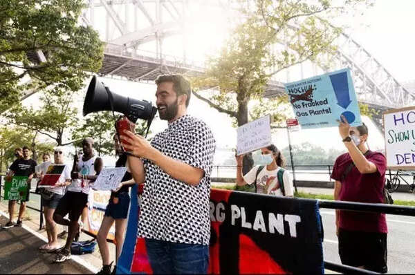 Zohran Mamdani advocating in Astoria, dressed in a smart casual style.